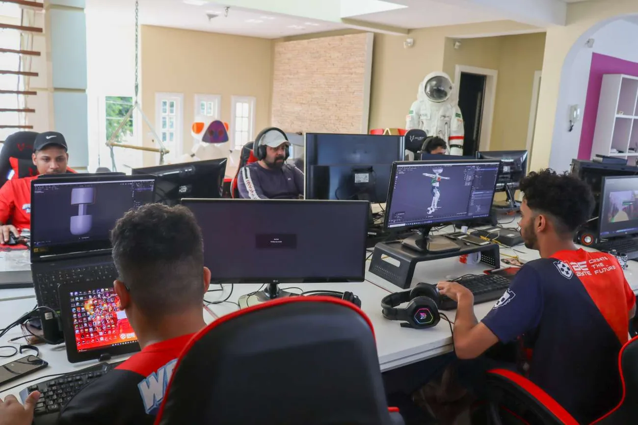 Jovens desenvolvedores trabalhando na Dev House da BeByte, com estações de trabalho, modelagem 3D e o astronauta ao fundo