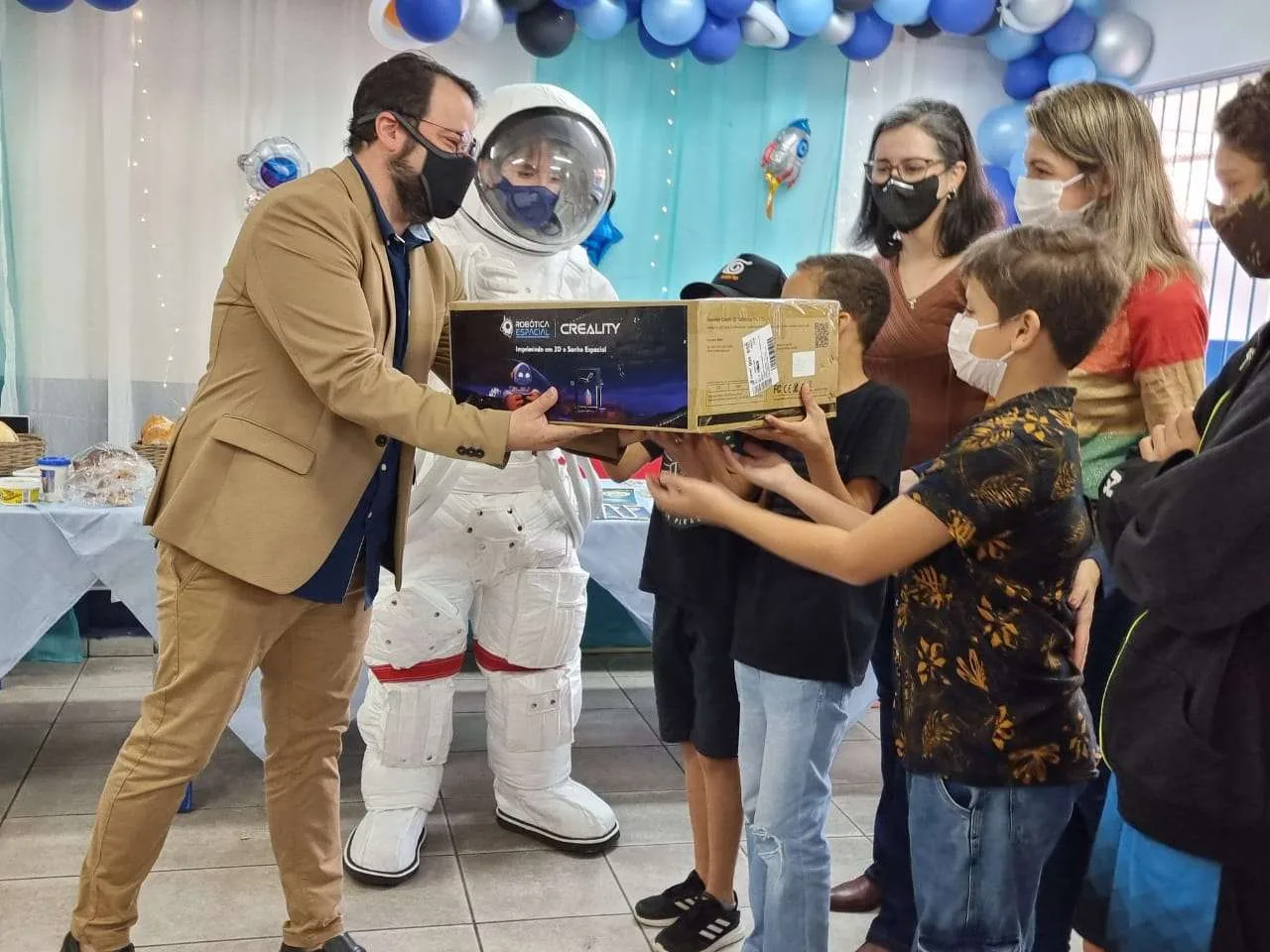 Entrega de impressora 3D Creality em escola pública, com o astronauta da Robótica Espacial e alunos segurando a caixa